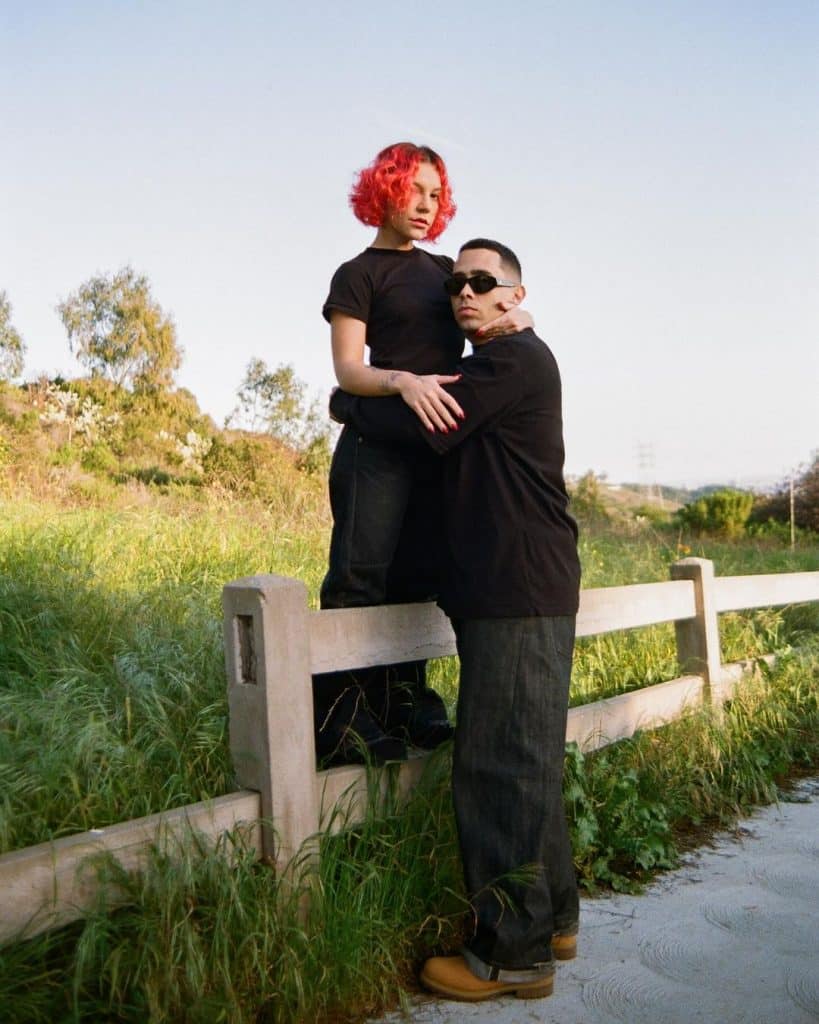 Priscilla e Andre abraçados em photoshoot, no mato, vestidos de preto.