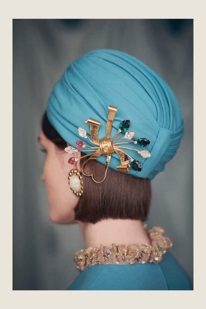 Modelo com turbante azul, na parte de trás há um broche dourado com pedrarias.